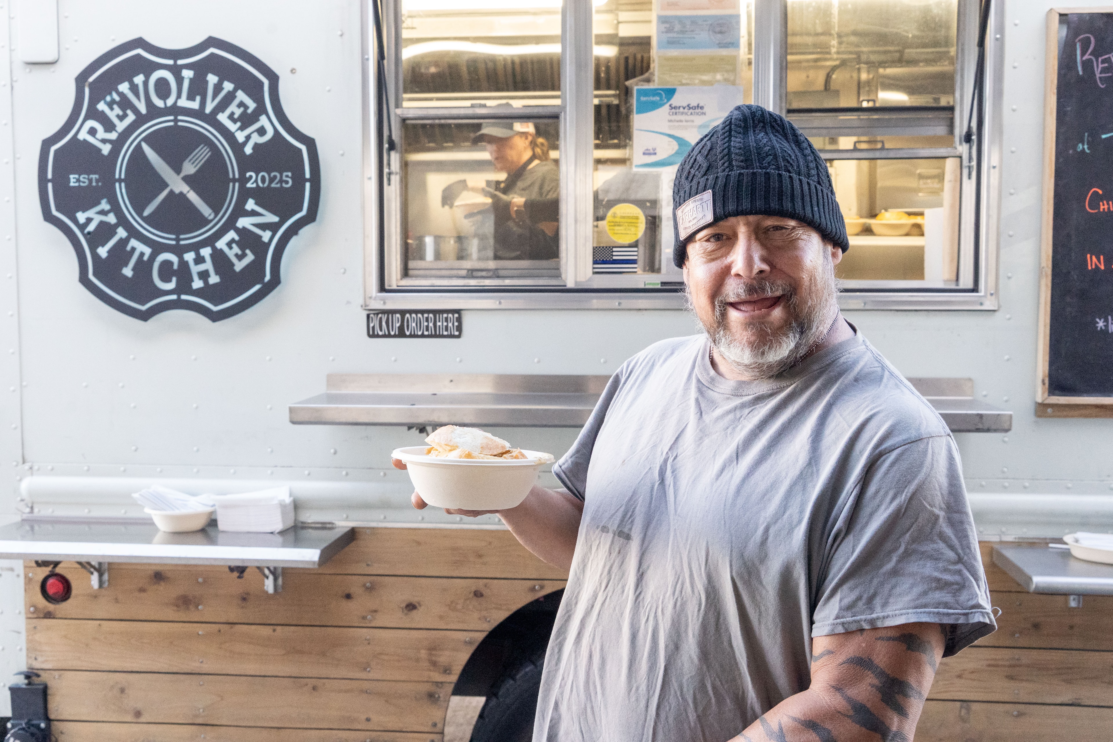 Happy customer holding a bowl of food in front of the Revolver Kitchen truck