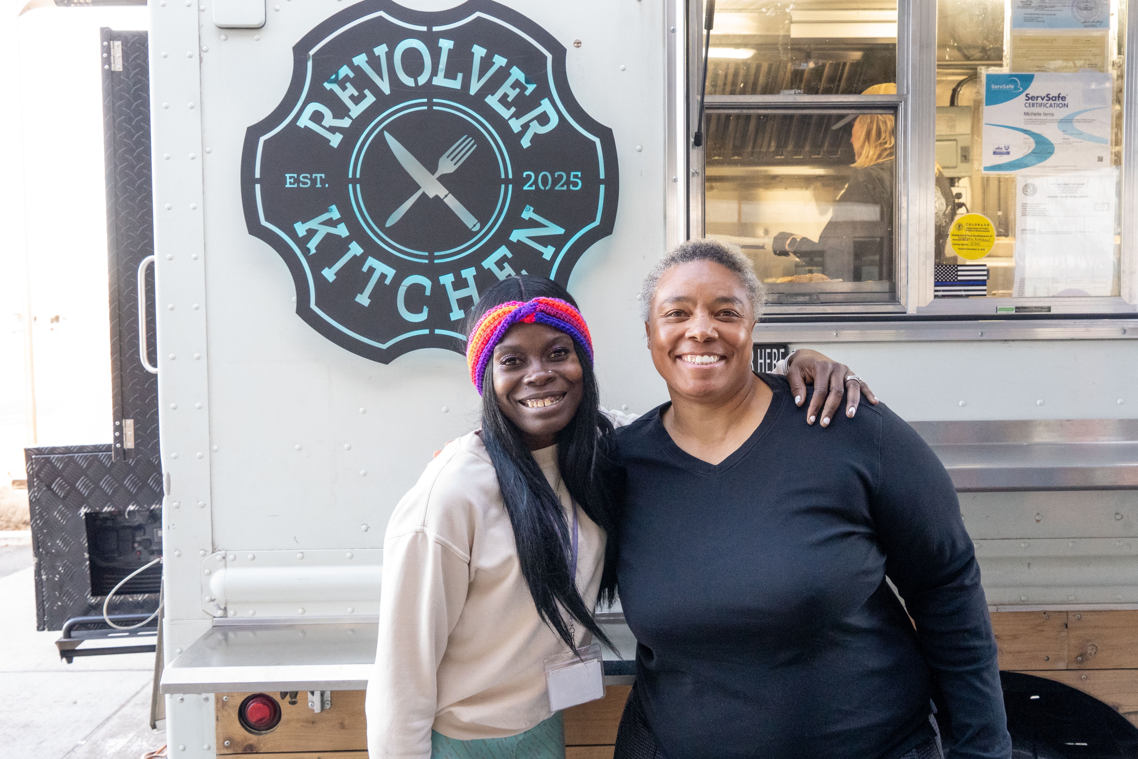 Two people smiling in front of the Revolver Kitchen sign